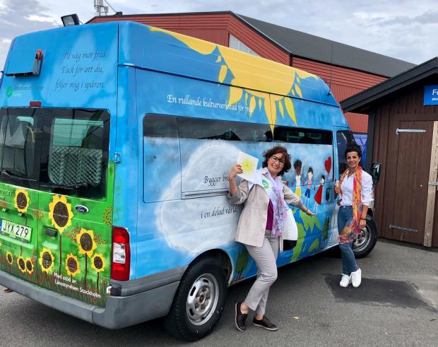 Two women pose by multicolored bus